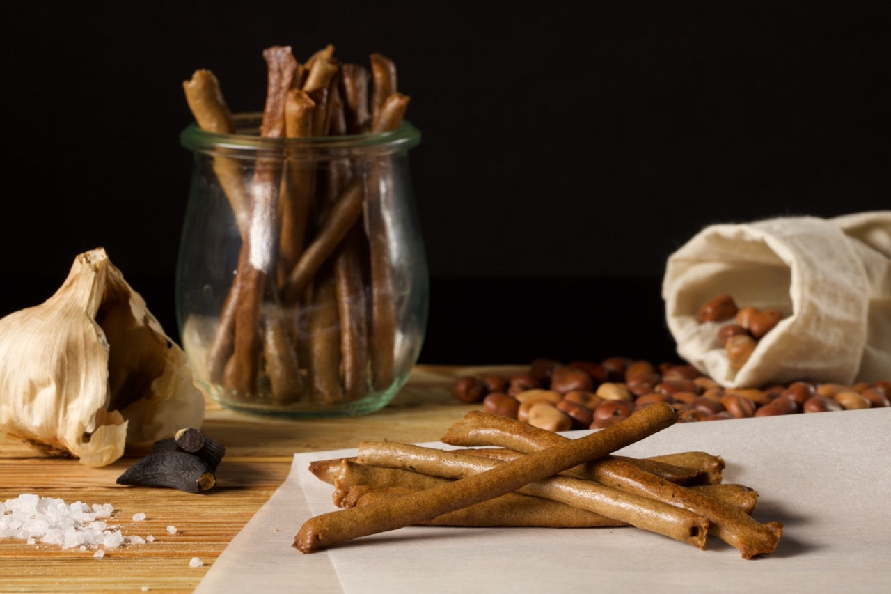 Ein rustikales Stillleben von LeSticca – 90 g Sauerkraut im Glas, verstreute Haselnüsse, eine Knoblauchknolle, Nelken und Meersalz auf einem Holztisch vor einem dunklen Hintergrund, mit Qio Food.