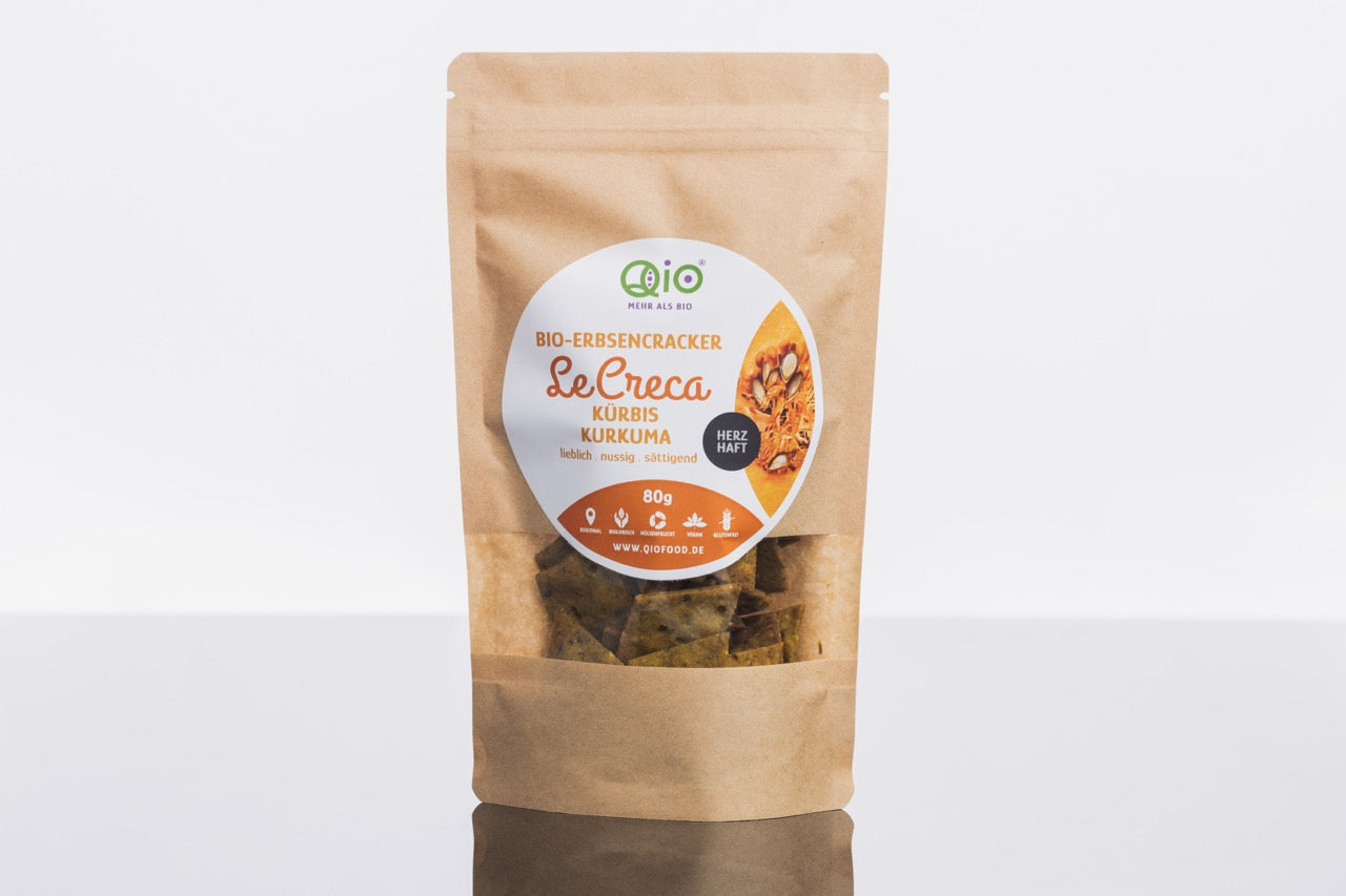 Ein aufrecht stehender brauner Papierbeutel mit der Aufschrift „LeCreca – Kürbis Kurkuma 80g“, gefüllt mit Bio-Kürbis- und Kurkuma-Crackern aus nachhaltig hergestellten Bio-Zutaten von Qio Food.