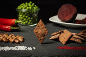 Eine Komposition aus ausgewogenen gesunden Lebensmitteln natürlichen Ursprungs mit einer Pyramide aus 80 g großen Crackern „LeCreca – Rote Bete Chilli“ von Qio Food, umgeben von Erbsen, Kichererbsen, roten Chilischoten, Meersalz und Paprika.